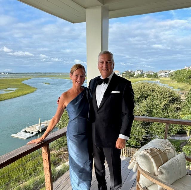 A couple in evening dress on a waterside deck, marsh and open water behind them