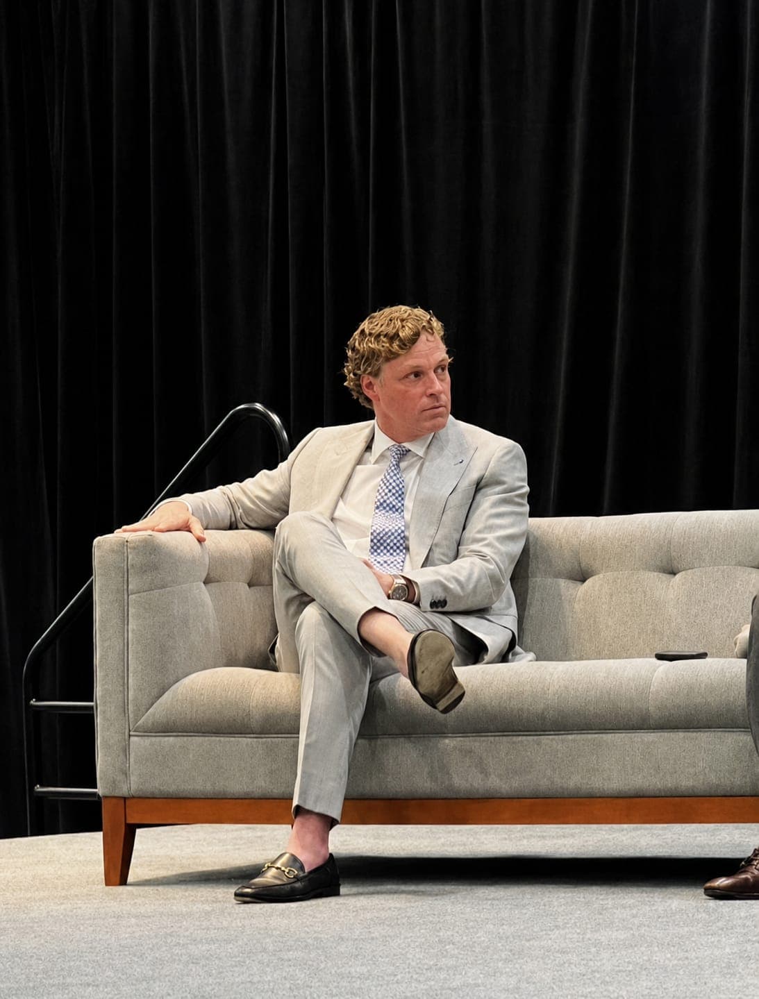 A client in a pale summer suit seated on a stage