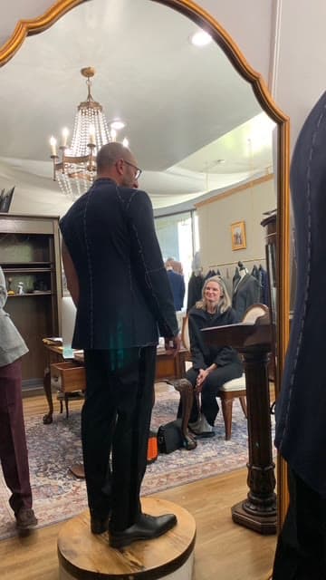 A rail of finished suits and shirts in a private fitting room, one drawn forward