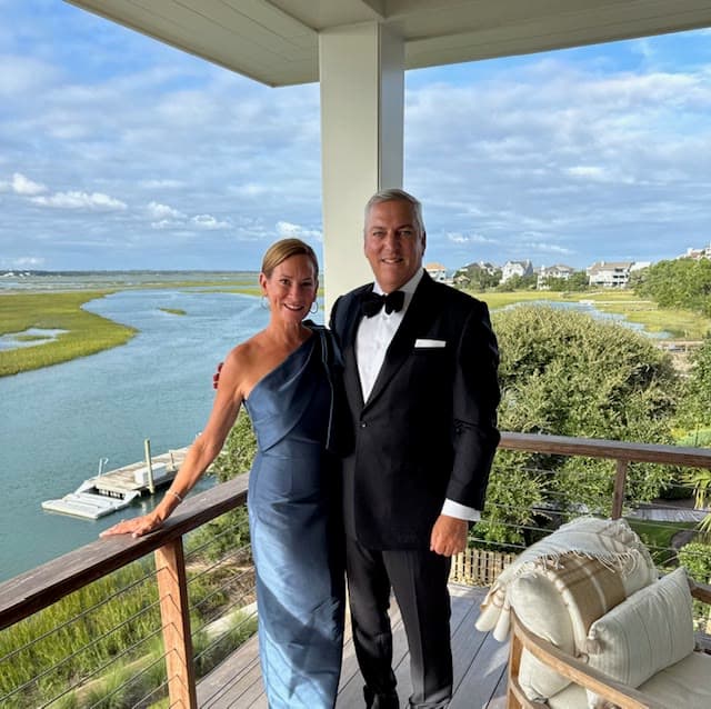 A couple in evening dress on a waterside deck, marsh and open water behind them