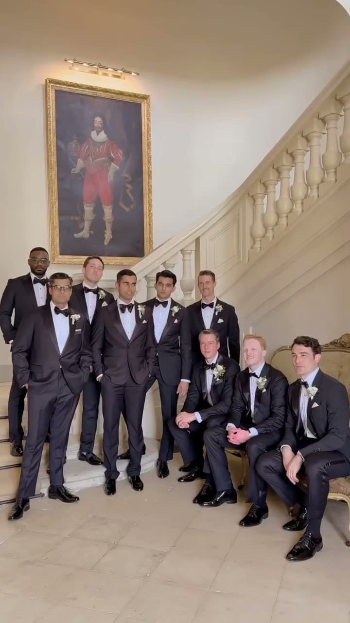 The groomsmen in black tie gathered on the château's stone staircase beneath a portrait